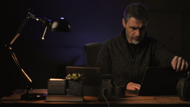 Business portrait - Businessman sitting at desk with laptop computer. Entrepreneur working late in home office. Older, middle aged, mid adult, man in his 40s or 50s in casual sweater.