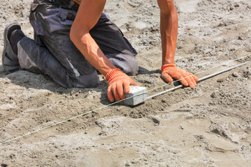 A worker sets a level with a stretched nylon thread to level the construction site before laying paving slabs.