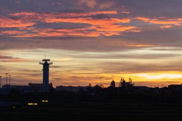 Silhouettes of the tower of houses and trees by the airfield at bright sunset