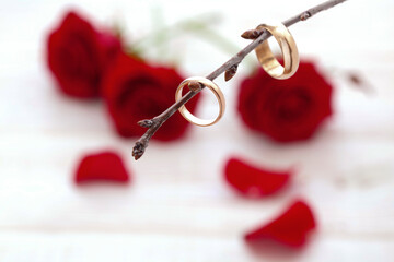 Wedding rings and many rose petals and a bouquet of red roses on white wooden desk