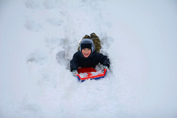 Fototapeta na wymiar Little boy sliding on a sled in the snow outdoors in winter.
