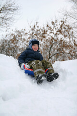 Fototapeta na wymiar A 6-year-old boy quickly descends a snowy hill on a sleigh.