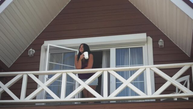 Girl goes out in the morning to the balcony with a cup of coffee