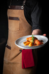 Delicious fried chicken in sauce with potatoes and rosemary on plate, the dish is hold in the hands...