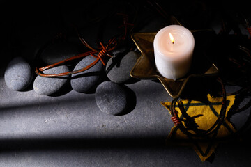 Holocaust memory day. Barbed wire, stones, yellow star and burning candle on black background