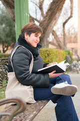 Obraz premium Woman with short hair reading a book sitting on a park bench