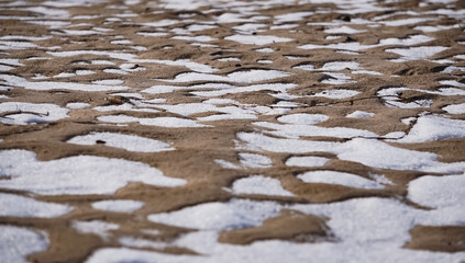 Chaotic snow spots on the beach in winter, sandy pits are filled with snow abstraction for the background