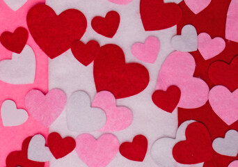 Valentine's Day themed background of red, pink and white hearts cut from felt fabric strewn randomly on strips of red, pink and white felt fabric.