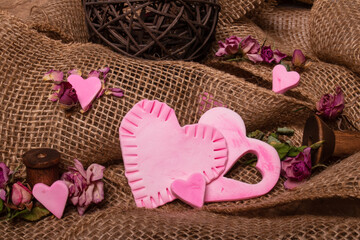 Valentine's Day themed studio shot of pink clay heart shapes arranged on a multi level burlap background with dried miniature roses scattered about.
