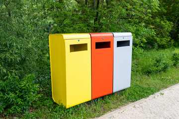 Multicolored metal containers for separate garbage collection in a public park. Environmental conservation, landscaping