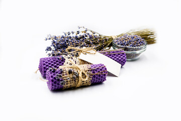 two violet lavender candles and  dry lavender flowers in glass plate with a bouquet of dry lavender on a white background