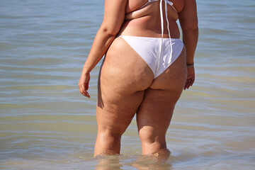 Overweight woman in white swimsuit going to swim in a water. Vacation on sea beach, overeating and...