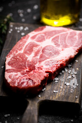 Raw pork steak on a cutting board with spices and rosemary. 