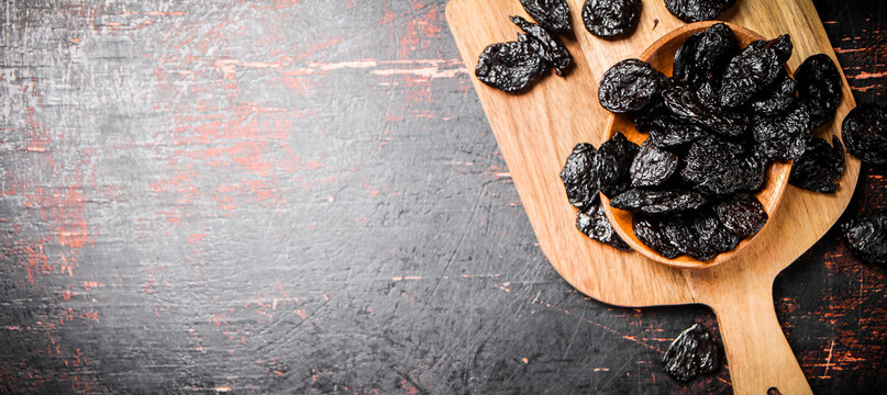 Prunes in a plate on a wooden cutting board. 