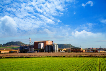 Beautiful landscape scenery with agro-processing and manufacturing plant and field under blue cloudy sky, Agricultural Silos - Building Exterior, Storage and drying of grains, wheat, corn, soy