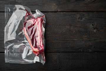 Raw beef meat Club or striploin on the bone steak in plastic airtight pack, on black wooden table background, top view flat lay, with copy space for text