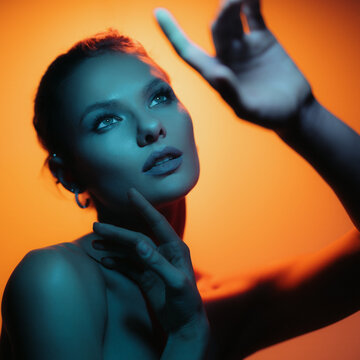 Fashion woman profile portrait on orange gradient background with soft blue light play on skin. Hands touching skin. Lights play.