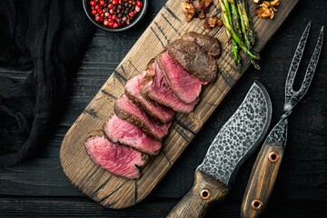 Juicy steak medium rare beef, tenderloin or fillet mignon cut, on wooden serving board, on black...