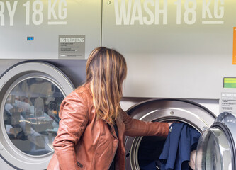 middle-aged woman in black dress and brown jacket, using self-service laundromat, introducing dirty clothes and using card payment, horizontal image, copy space