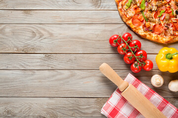 Pizza, tomatoes, mushrooms, bell pepper and rolling pin on wooden table background. Top view with...