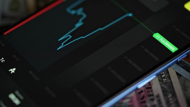 Buying stocks in the investment market in close-up. Checking data in the financial market. Using your phone to analyze a rising stock fund. Displaying a stock market chart on a touch screen monitor.