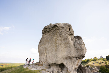 Kids exploring nature. Children wear backpack hiking with mother near big stone in hill. Pidkamin, Ukraine.