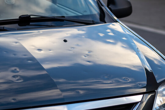 Black car engine hood with many hail damage dents show the forces of nature and the importance of car insurance and replacement value insurance against hail dents of storm hazards extreme weather