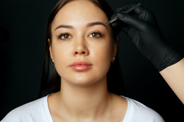 Fototapeta na wymiar Cosmetician correcting woman's eyebrows with a tweezers