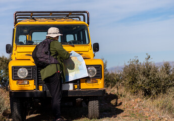 middle-aged woman in green shirt, driving yellow 4x4 in the mountains and looking at a map.horizontal image, copy space, concept of adventure, experiences. © La_maca