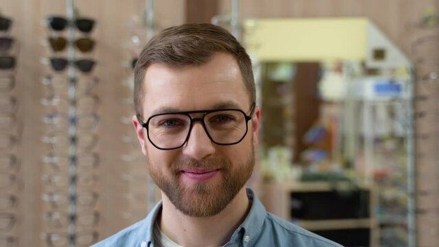 Portrait of handsome bearded guy picking new specs at optical shop, looking at camera. Choosing Glasses Concept