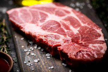 A steak of raw pork on a cutting board with tomato sauce and rosemary. 