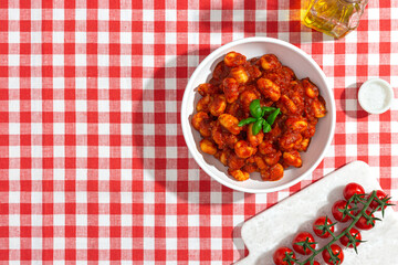 gnocchi with tomatoes and basil on a red checkered tablecloth top view