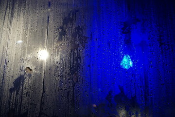 Abstraktes Motiv mit feuchter beschlagener grau-blaue Plastikfolienwand mit Wasser- und Lichtmuster bei Nacht im Winter