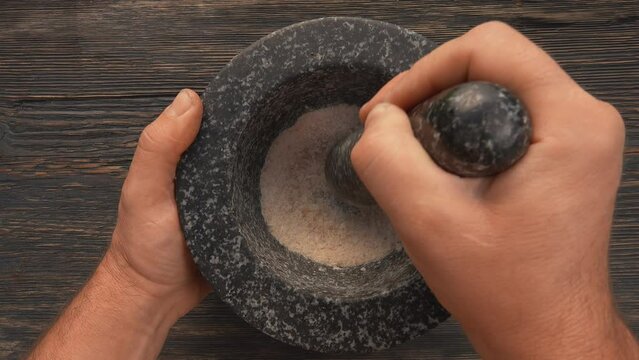 A man's hand grinds a mixture of salt sugar lemon zest in a stone mortar