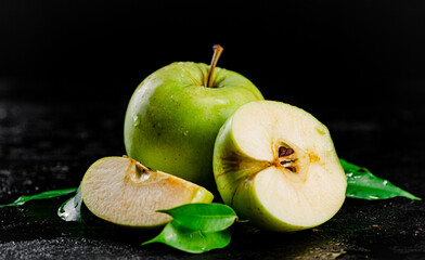 Pieces and a whole apple with leaves on the table. 