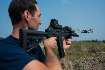 A man aims to shoot a rifle at a flying drone against a blue sky. 