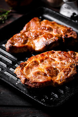 Cooked pork steak in a frying pan grilled with rosemary. 