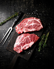 Raw pork steak on a cutting board with rosemary. 