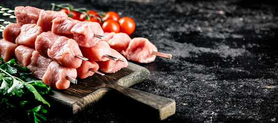 Pork kebab raw on a cutting board with tomatoes and parsley. 