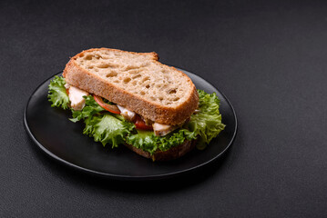 Fresh tasty sandwich with chicken, tomatoes and lettuce on a black plate