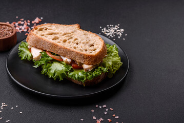 Fresh tasty sandwich with chicken, tomatoes and lettuce on a black plate