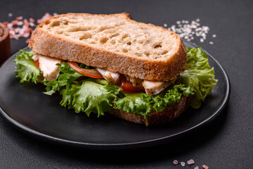 Fresh tasty sandwich with chicken, tomatoes and lettuce on a black plate