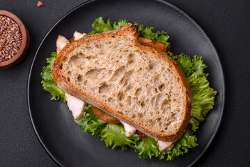 Fresh tasty sandwich with chicken, tomatoes and lettuce on a black plate