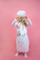 Little cook girl in an apron and cap, holds a glass cup and covers her face.The concept of food, restaurant, training, poster, postcard, health, diet, nutrition,copy space, layout, hobby,job,childhood