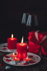 Saint Valentine's Day celebration. Red burning candles, hearts, gift box, postcard on dark wooden background. Happy holiday . Table decor for festive dinner, romantic atmosphere. Copy space for text