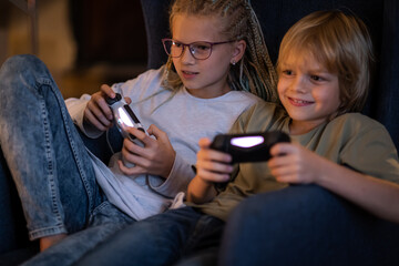 boy and girl playing video game console using joystick or controller while sitting at home, Two children small caucasian brother and sister happy children siblings, real people family leisure concept.