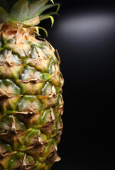 Vertical stock photo of half a whole pineapple with part of green leaves on a black 