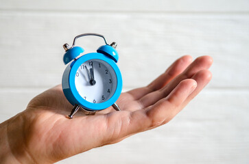 Classic arrow blue alarm clock on a man hand on white background, concept of the passage of time