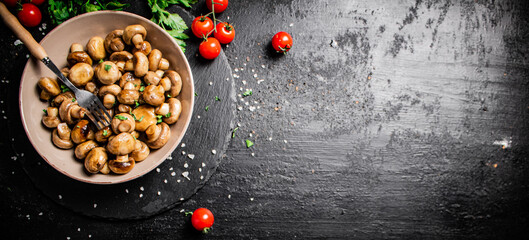 Fried mushrooms in a bowl with greens and tomatoes on a stone board. 