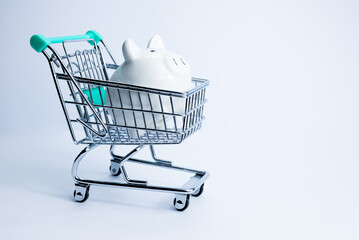 Empty grocery cart with white piggy bank on white background. Concept of the economic crisis. Inflation. Food shortages, food crisis, famine problems. Inflation 2023.